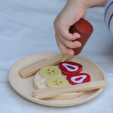 Child's hand holding a pretend sauce bottle above a waffle with topping from the PlanToys waffle play set