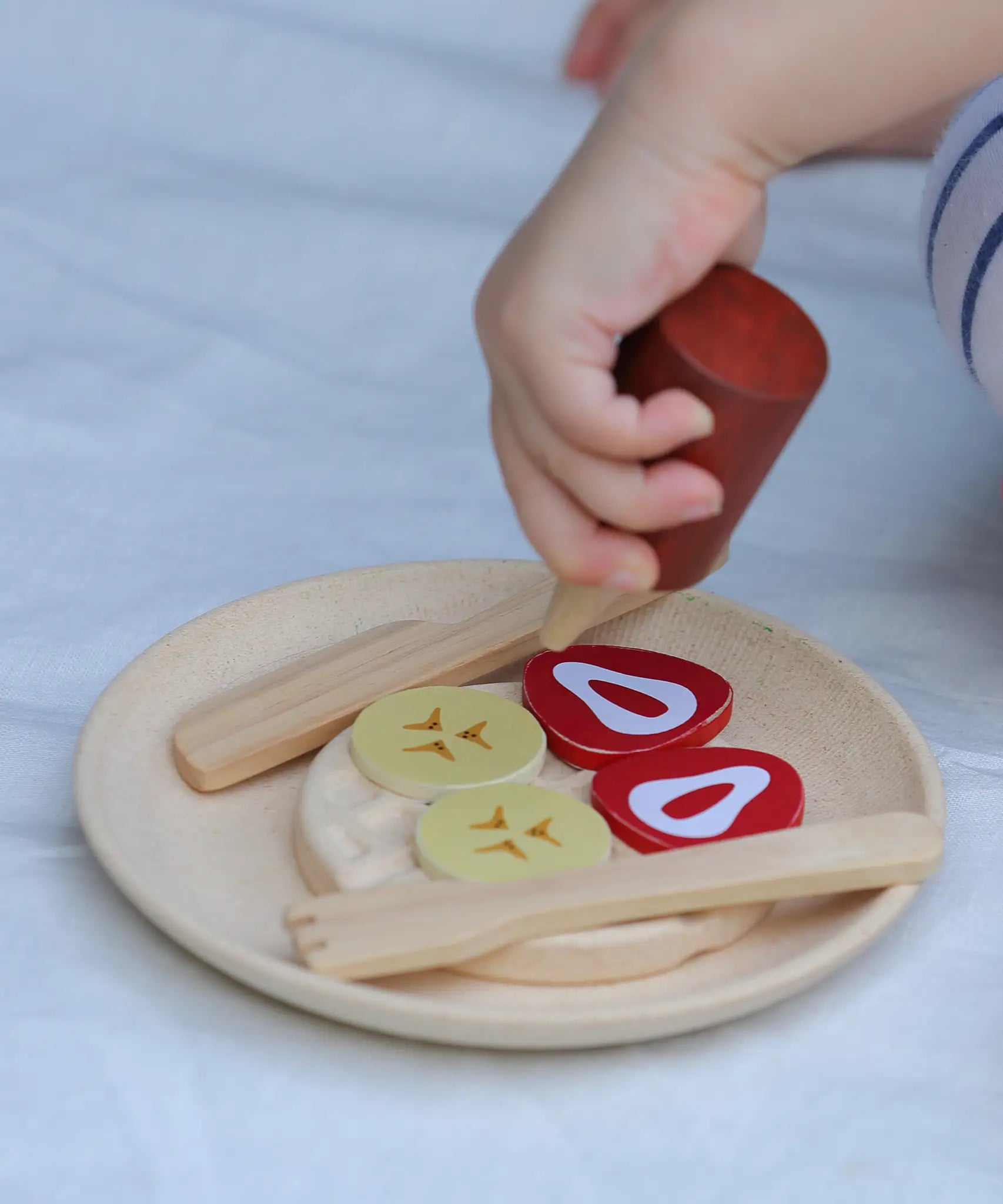 Child's hand holding a pretend sauce bottle above a waffle with topping from the PlanToys waffle play set