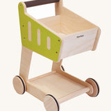 PlanToys Shopping Trolley is a fun, wooden kid size trolley with green sides and a brown handle. This trollwy is fun for storing play food and can also e used in shopping role play.  The image is on a cream background