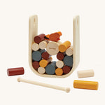 The PlanToys Giant Beaver Tumble is a fun kids game of strategic thinking and hand-eye coordination, using the wooden stick to push out the logs without the beaver falling. There is a large natural wood U shaped base to keep the sticks and beaver upright, and the sticks are in various sizes and colours such as yellow, brown, white and grey. The little beaver piece is orange with a black tal. The image is on a cream background.
