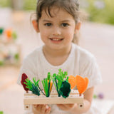 Child holding planter pieces with different veg pieces on top from  the PlanToys wooden blooming greenhouse 