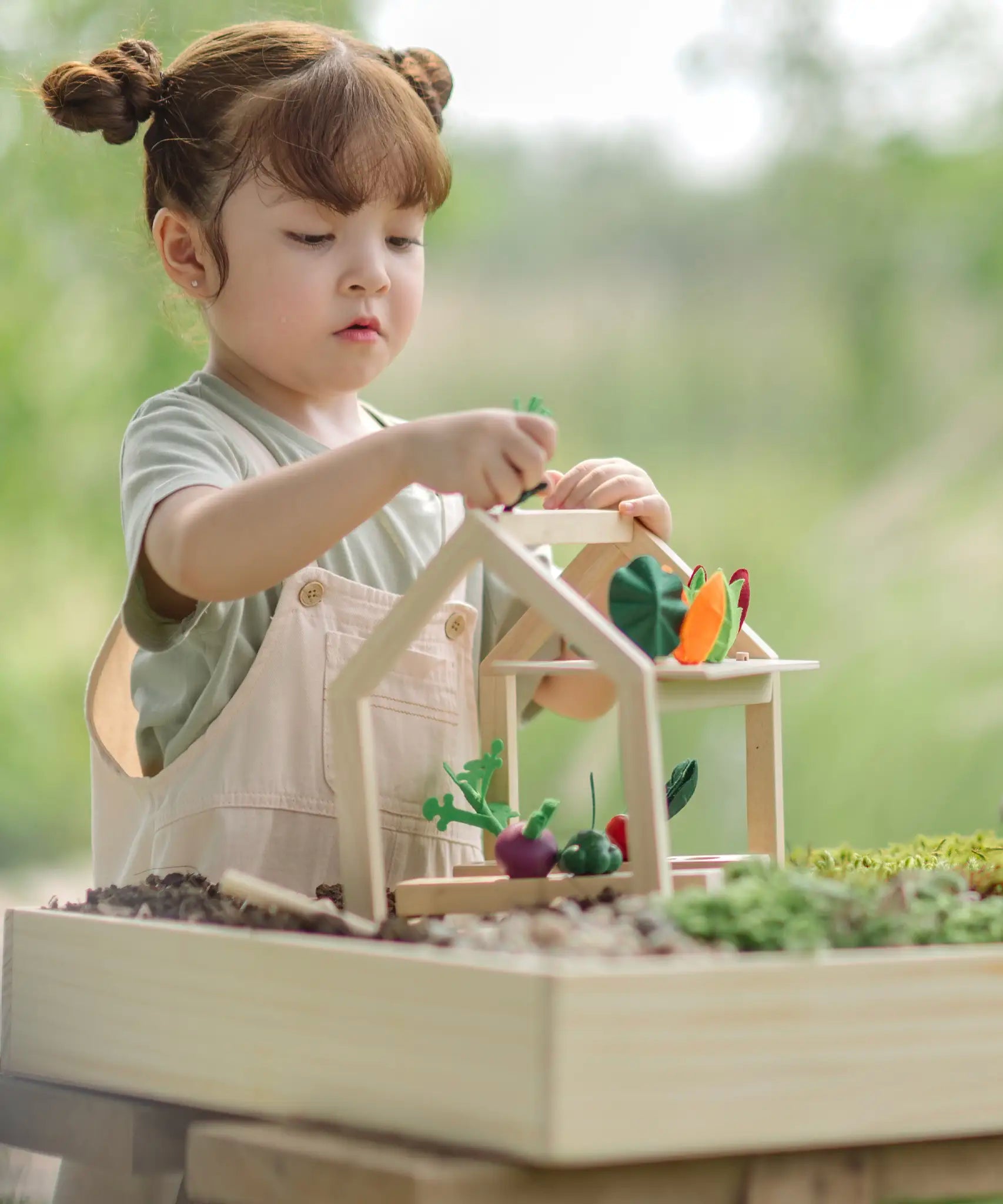Child sorting different veg pieces on the  planters and shelf pieces in the PlanToys wooden blooming greenhouse 