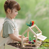 A PlanToys wooden blooming greenhouse standing on soil with a child sorting different veg pieces