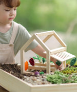 Child removing a veg piece from the planter inside the PlanToys wooden blooming greenhouse 