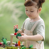 Child standing next to stacked planting beds from the PlanToys stack & sprout set and holding a loose veg piece