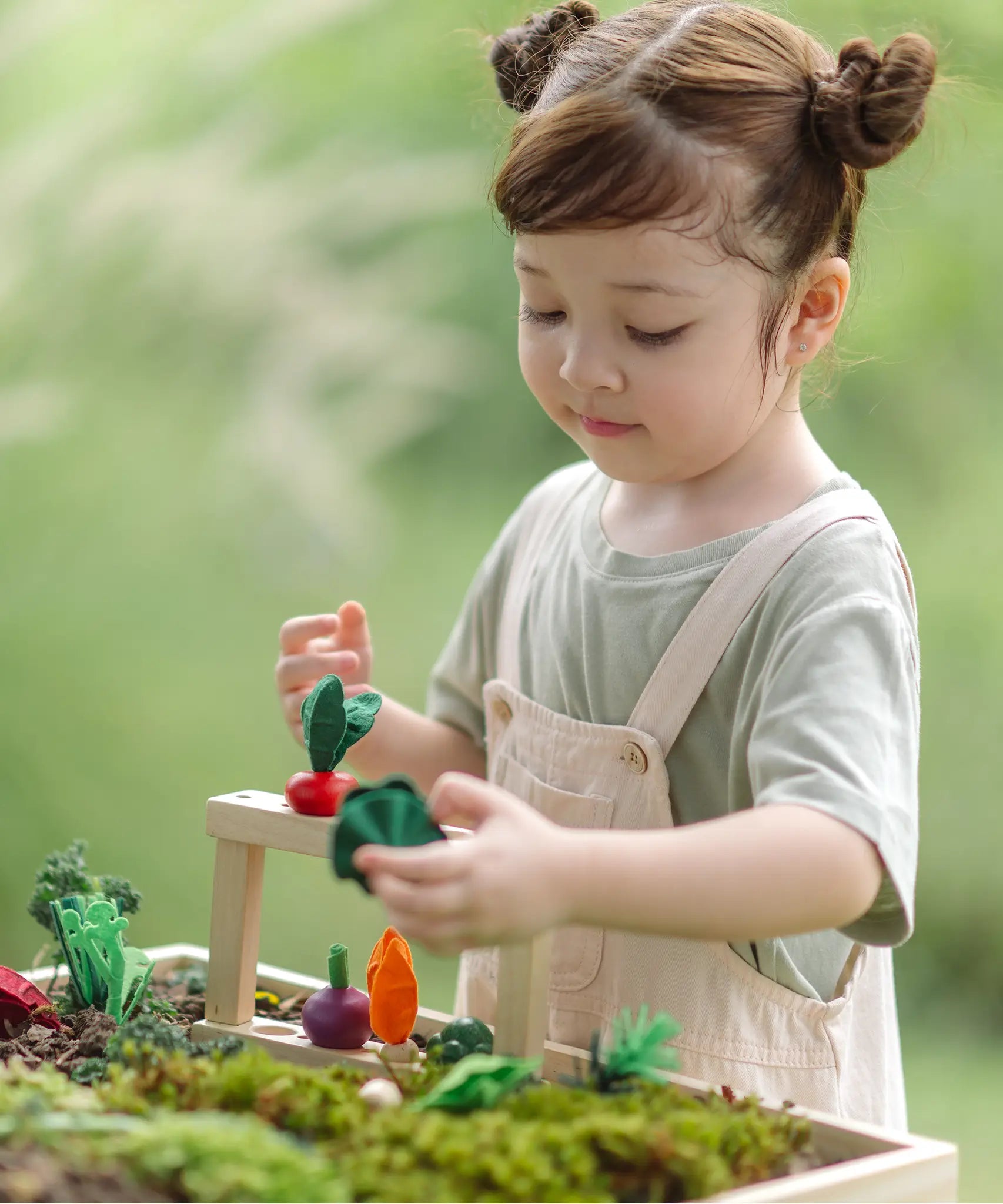 Child standing next to stacked planting beds from the PlanToys stack & sprout set and holding a loose veg piece