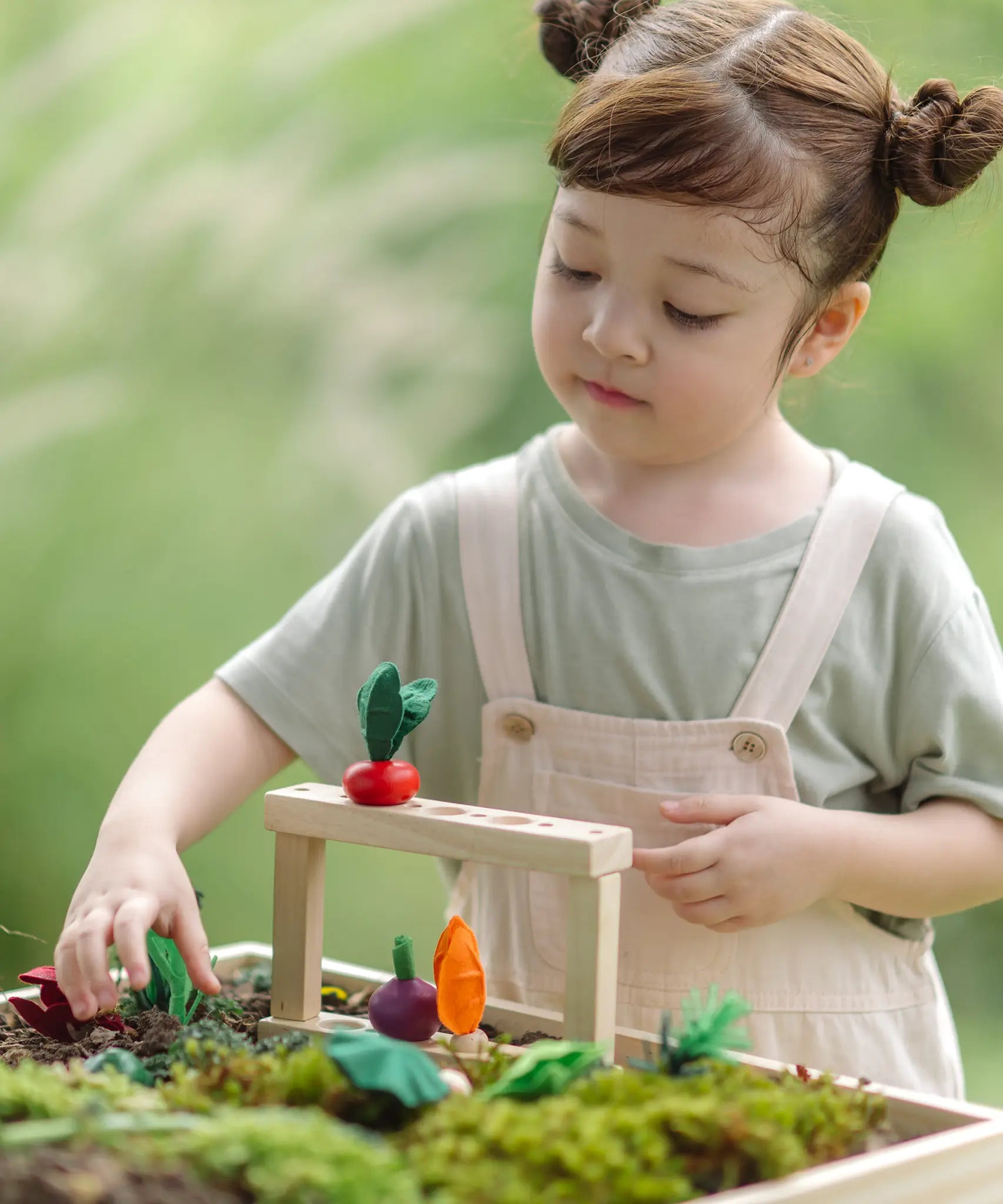 Child standing next planting beds from the PlanToys stack & sprout set with loose veg sitting on top