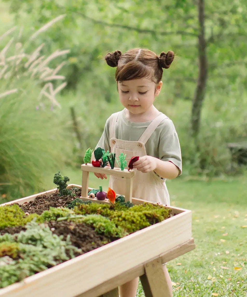 Child standing next to stacked planting beds from the PlanToys stack & sprout set with loose veg sitting on top in a garden