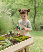 Child standing next to stacked planting beds from the PlanToys stack & sprout set with loose veg sitting on top in a garden