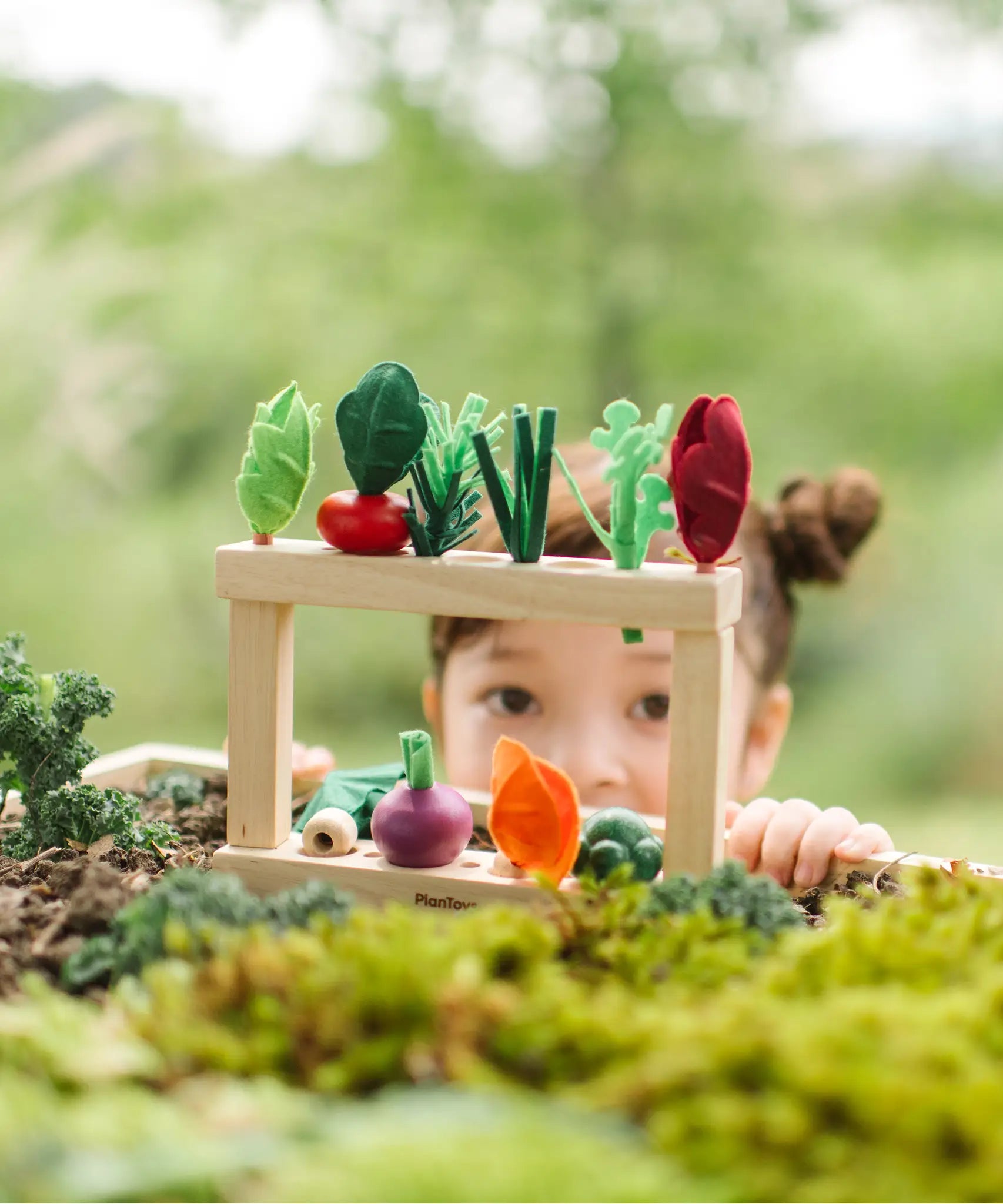 2 PlanToys wooden planting beds stacked using connecters with veg pieces sitting on top with a child standing behind