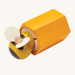 PlanToys Buzz Bee is a wooden grip and pull toy which zooms back into the bee hive once pulled. The hive is yellow, and the bee is yellow and black with cream wings. The image is on a cream background