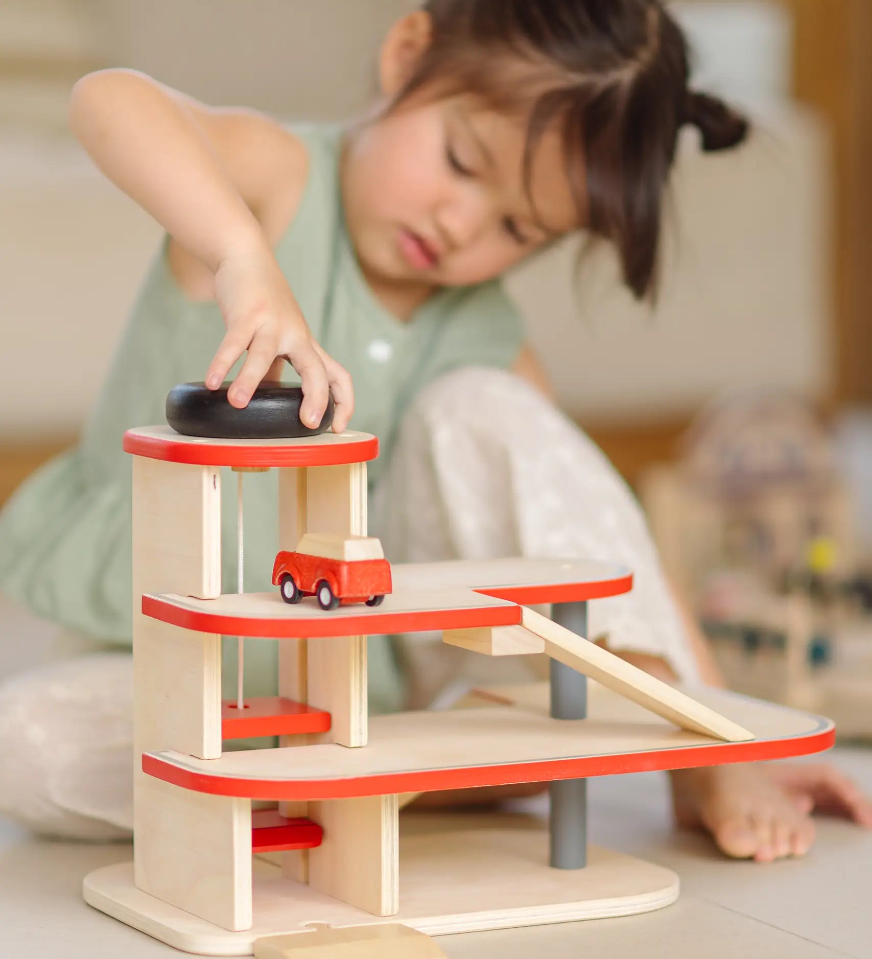 Child playing with the PlanToys wooden city parking garage using the wind up vehicle working lift