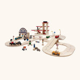 PlanToys city transit with rail and road playset showing different wooden vehicles on the rail and road pieces with a car park in the background