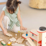 Child holding on loose PlanToys wooden road pieces next to a car park from the city transit rail road playset