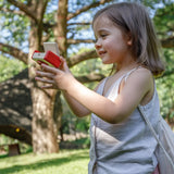 Child holding a camera from the PlanToys vlogger kit on a grassy field