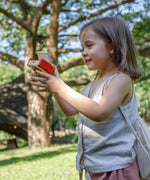 Child holding a camera from the PlanToys vlogger kit on a grassy field