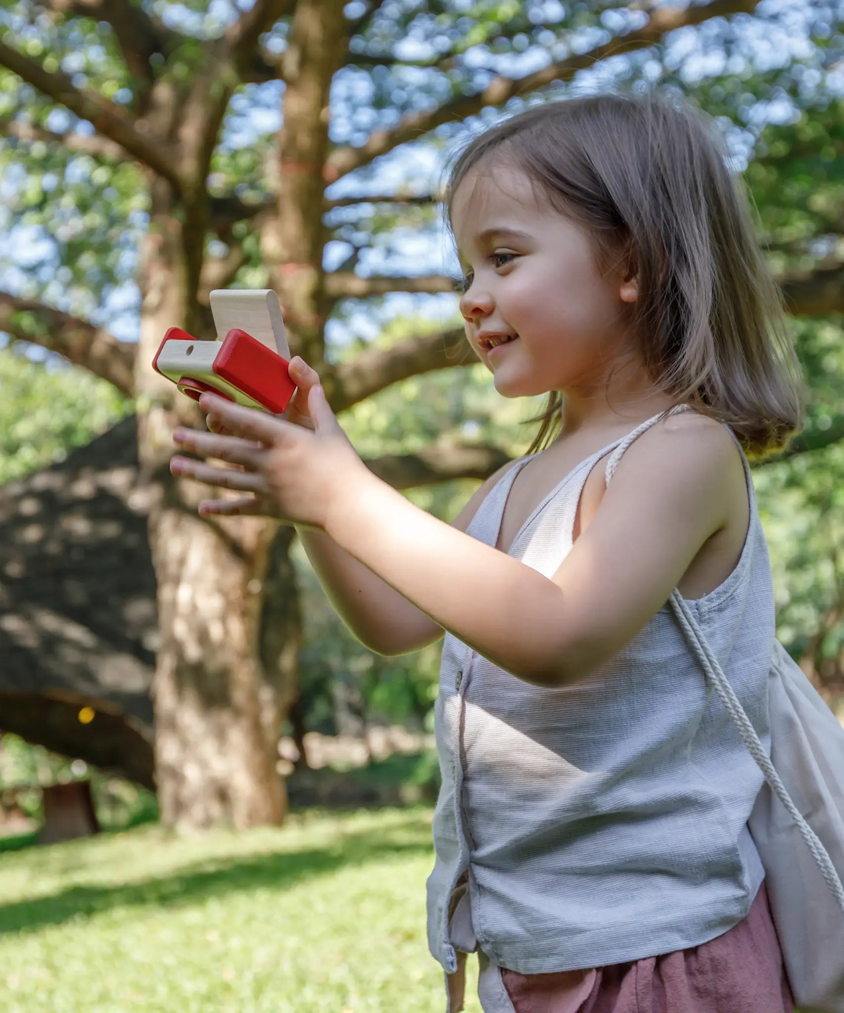 Child holding a camera from the PlanToys vlogger kit on a grassy field