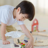 Child playing with the market stall set next to a PlanToys wooden roadway