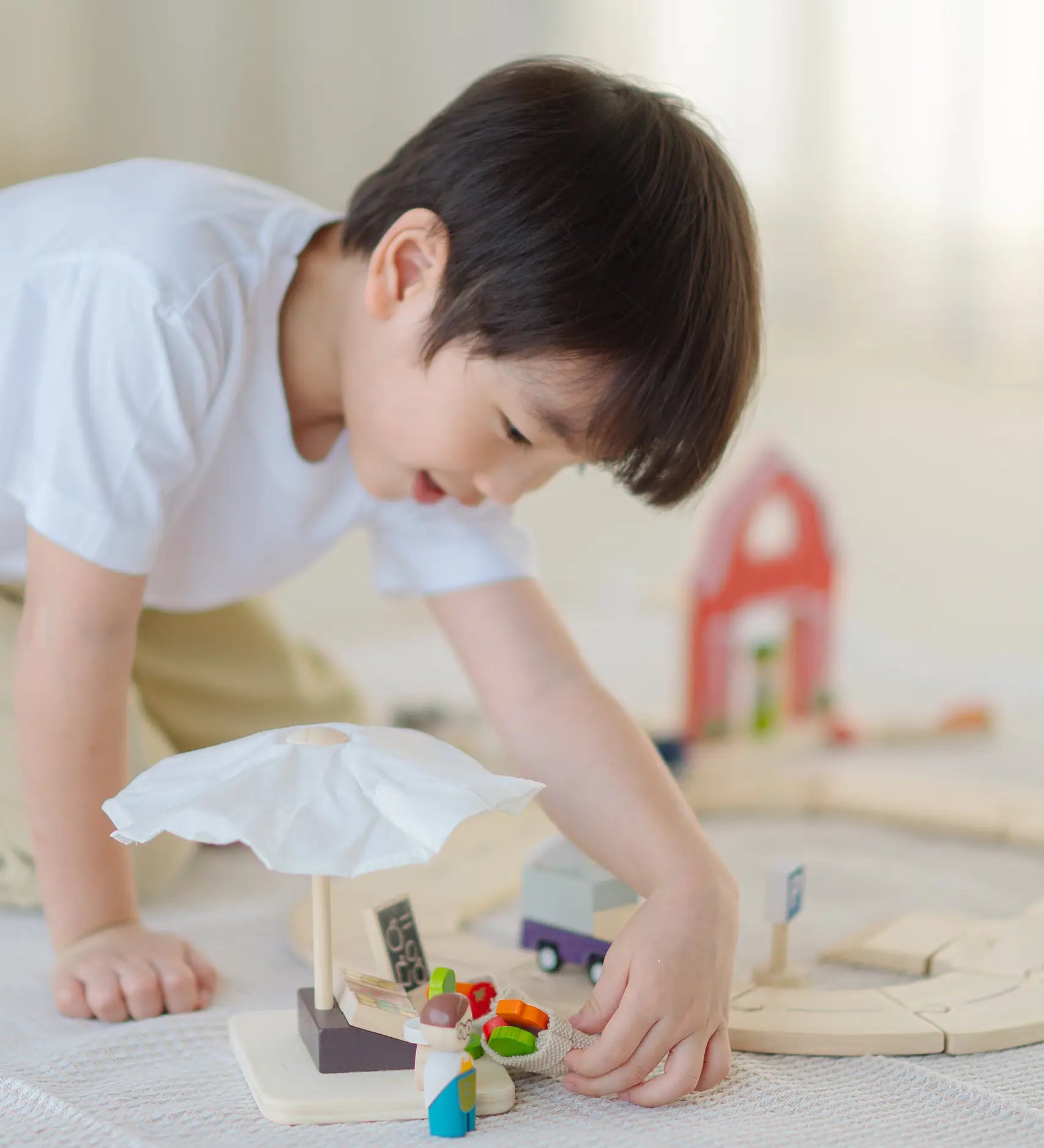 Child playing with the market stall set next to a PlanToys wooden roadway