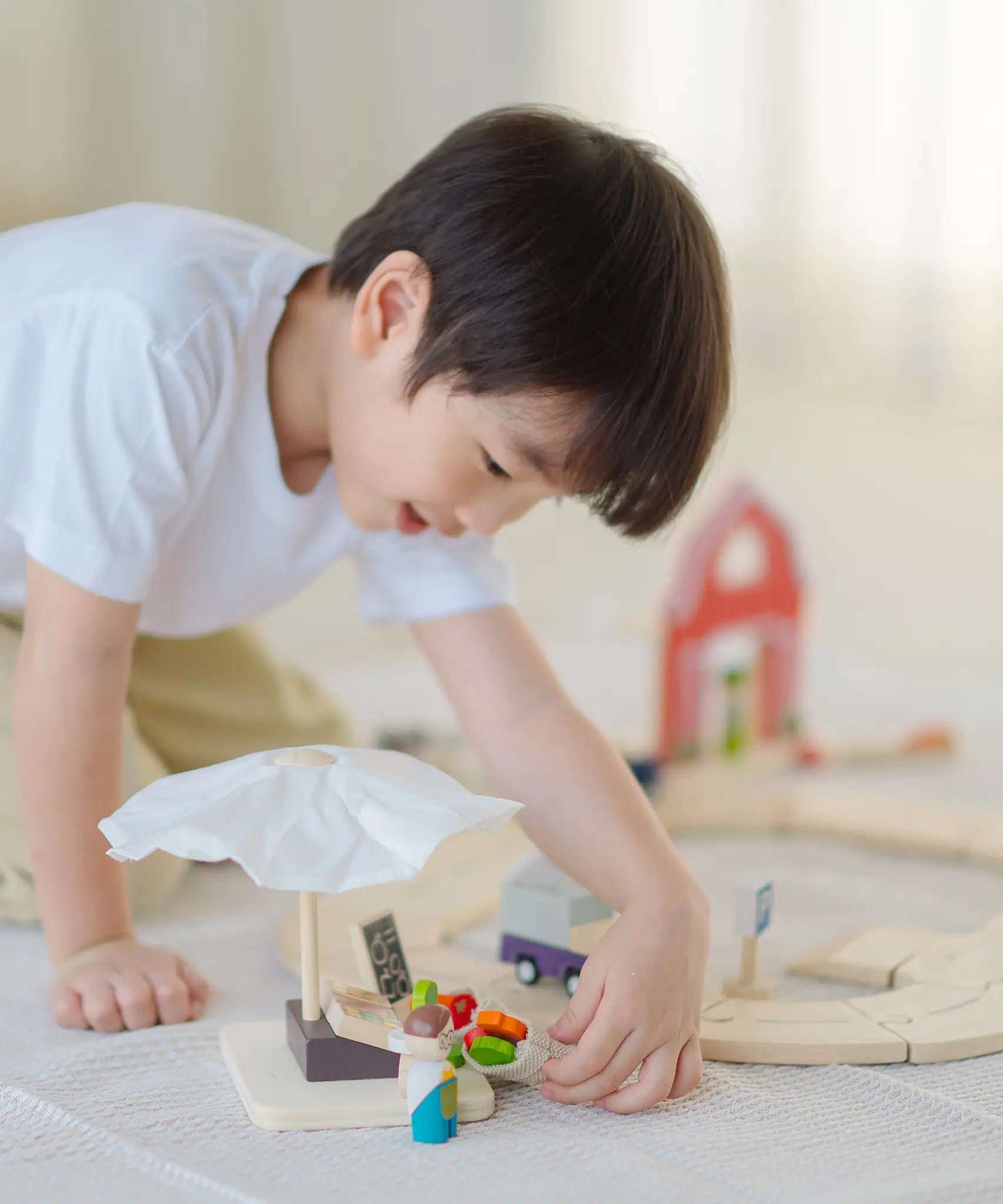 Child playing with the market stall set next to a PlanToys wooden roadway