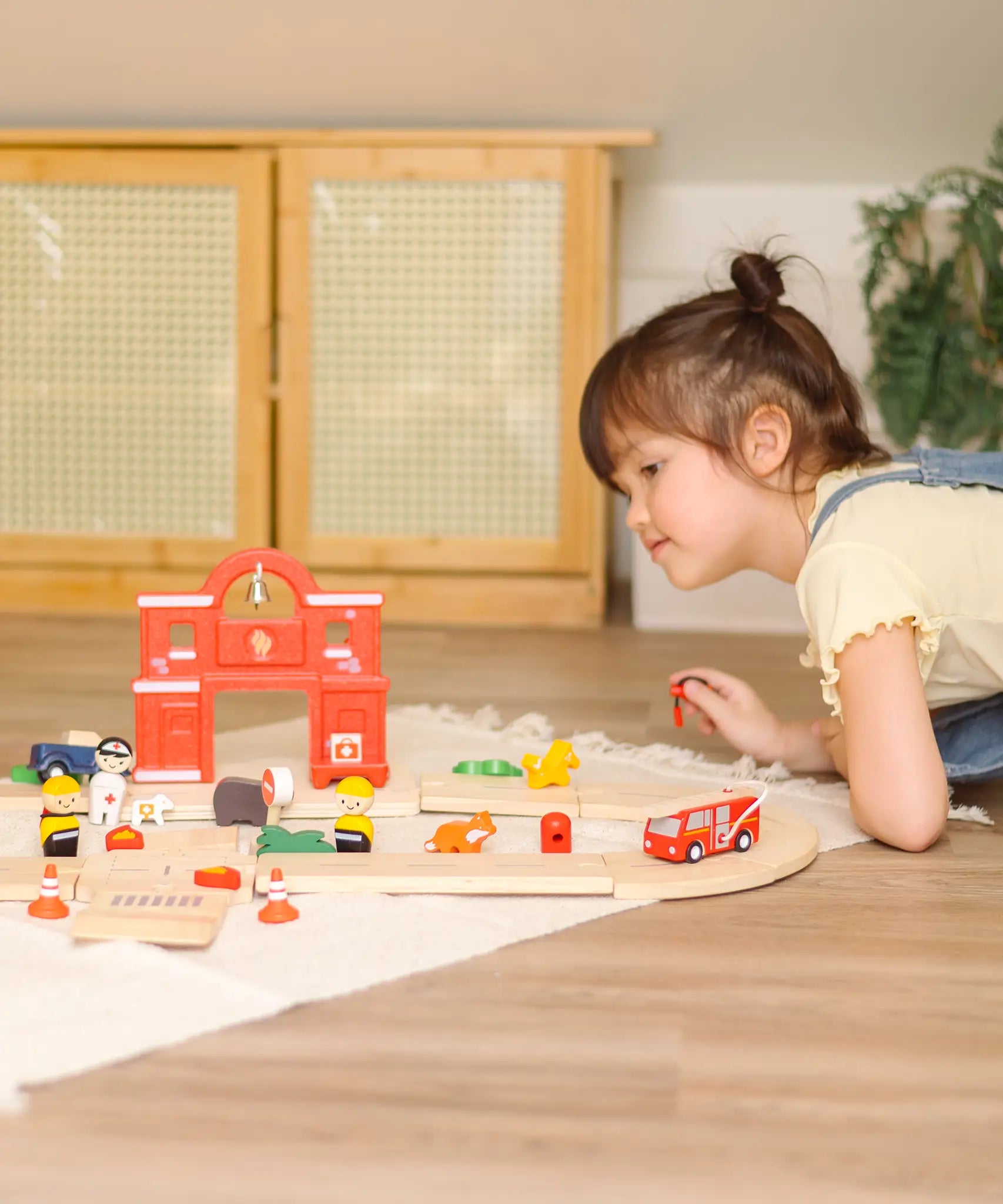 Child leaning over a Child playing with the PlanToys fire & rescue roadway set on a rug