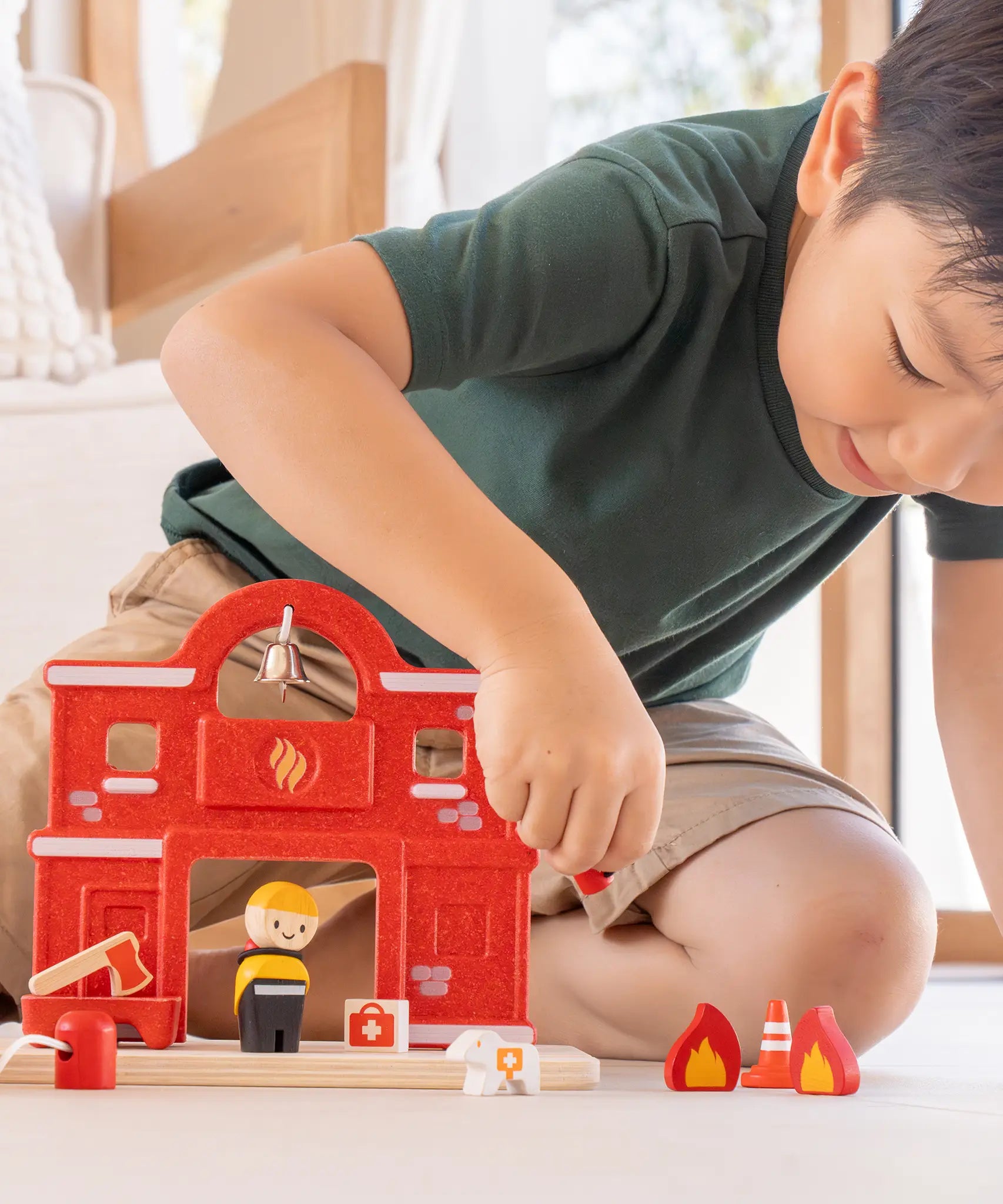 Child playing with the PlanToys fire station extension set showing a fireman figure and other related pieces