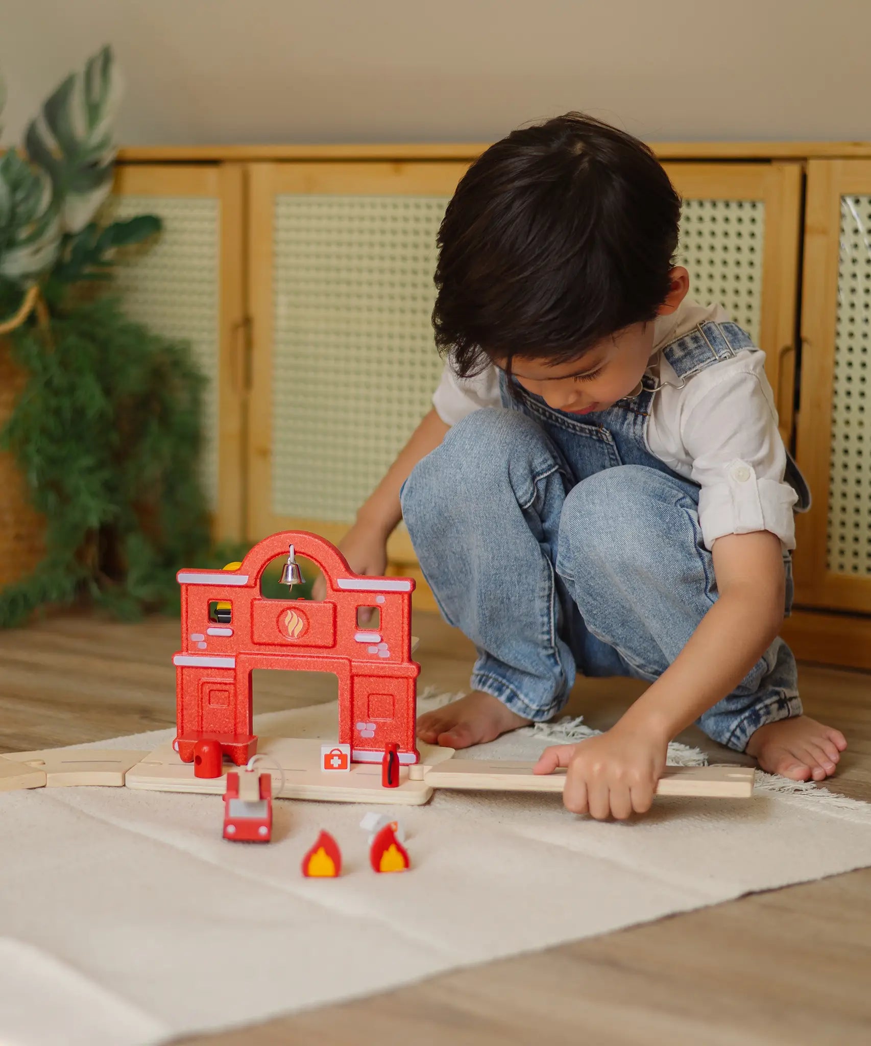 Child connecting a loose PlanToys road piece with the fire station extension set