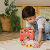 Child placing a small cone in front of a PlanToys fire station and road setup