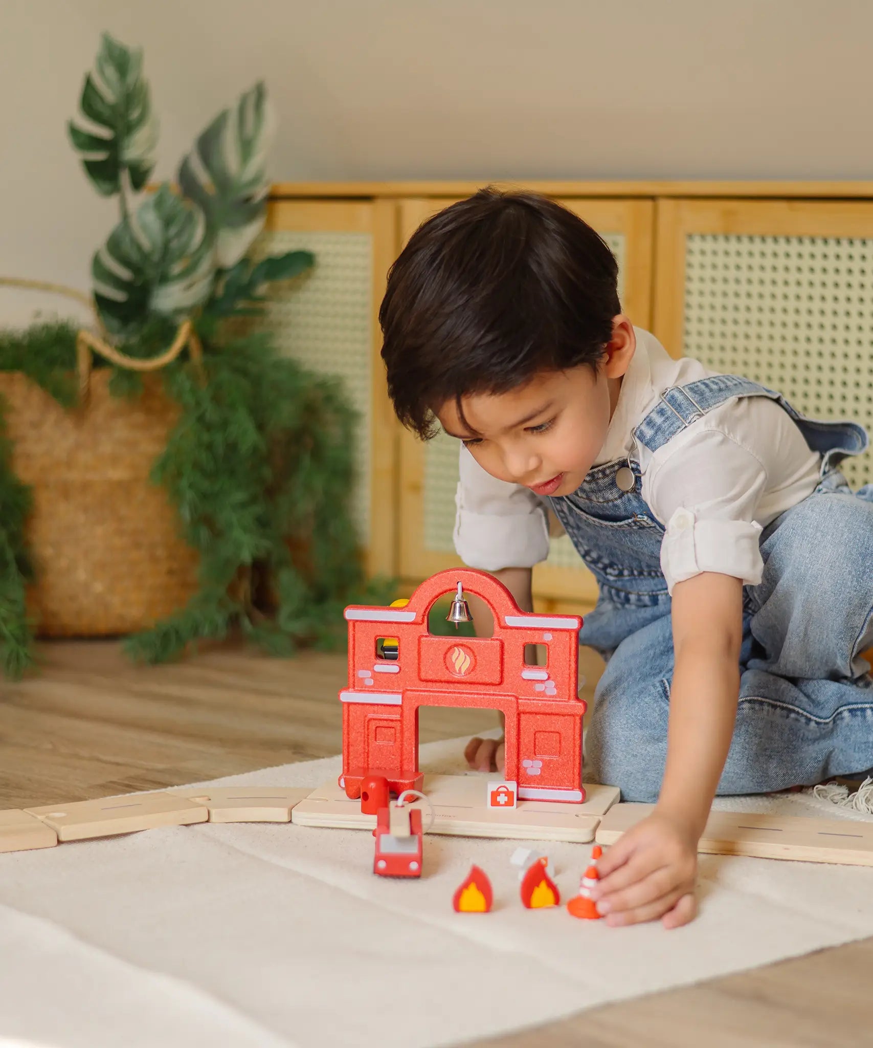Child placing a small cone in front of a PlanToys fire station and road setup