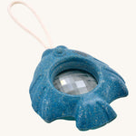 The PlanToys Fish Kaleidoscope is a fun blue kaleidoscope toy in the shape of a fish, with a beige rope handle and a circle in the middle of the fish with the lens. The image is on a cream background