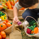 Child holding a loose wooden turnip piece with a PlanToys basket filled with other veggie pieces