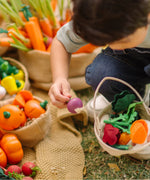 Child holding a loose wooden turnip piece with a PlanToys basket filled with other veggie pieces