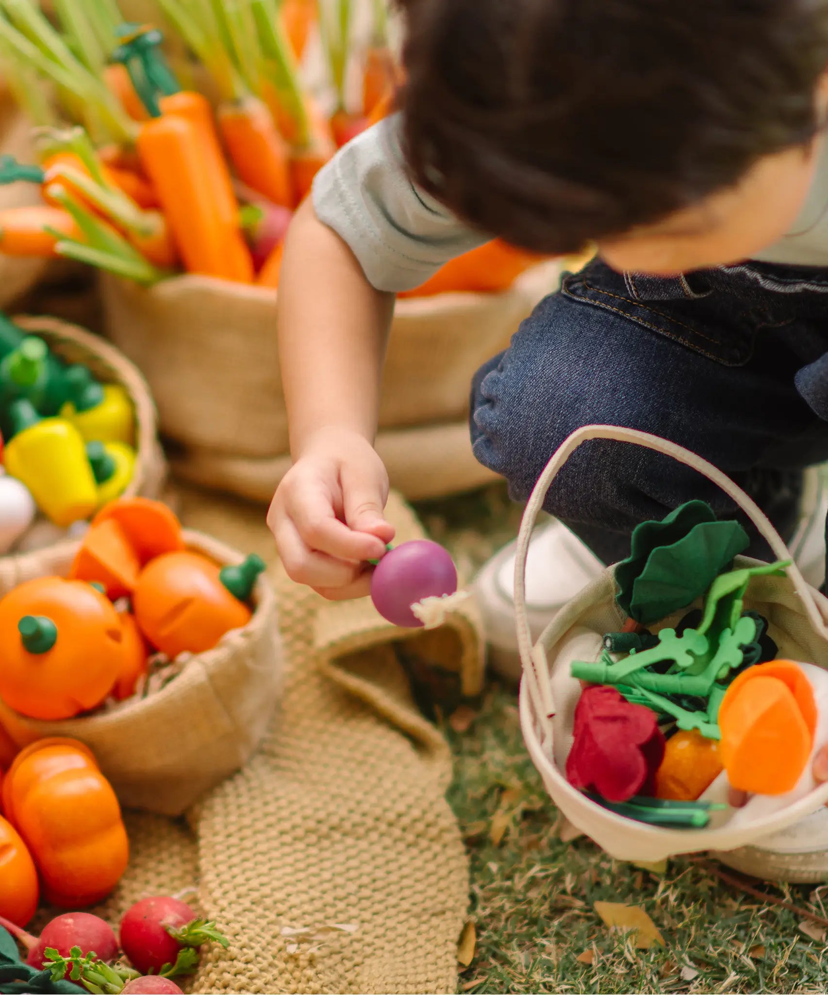 Child holding a loose wooden turnip piece with a PlanToys basket filled with other veggie pieces
