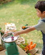 Child carrying a basket filled with wooden veggie pieces and placing some on scales