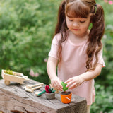 Child playing with the PlanToys garden wheelbarrow set with a orange bucket filled with soil 