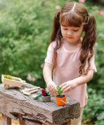 Child playing with the PlanToys garden wheelbarrow set with a orange bucket filled with soil 