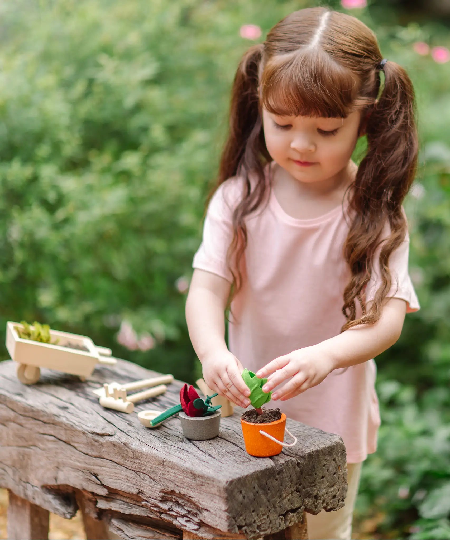 Child playing with the PlanToys garden wheelbarrow set with a orange bucket filled with soil 