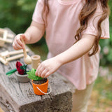Child filling a orange bucket from the PlanToys garden wheelbarrow set with soil on a wooden bench