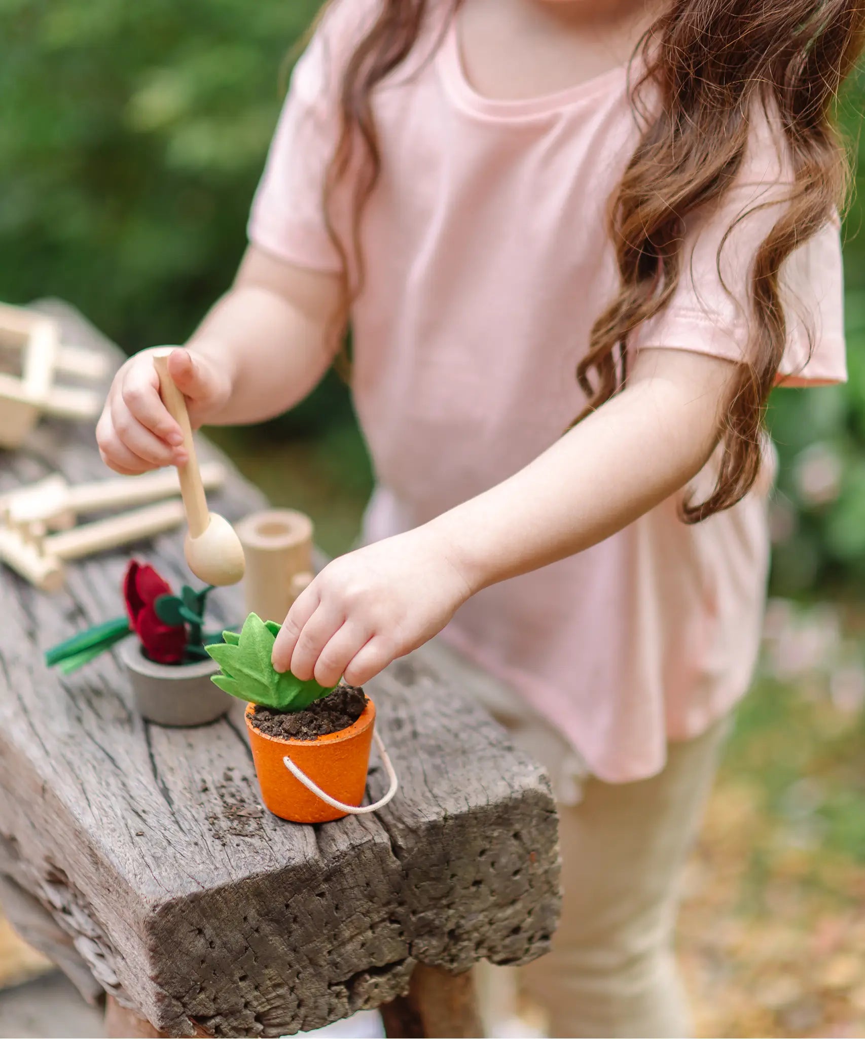Child filling a orange bucket from the PlanToys garden wheelbarrow set with soil on a wooden bench