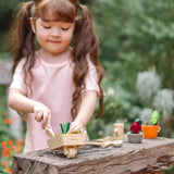 Child playing with a PlanToys garden wheelbarrow set on a wooden bench. 