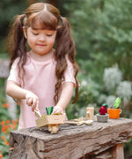 Child playing with a PlanToys garden wheelbarrow set on a wooden bench. 