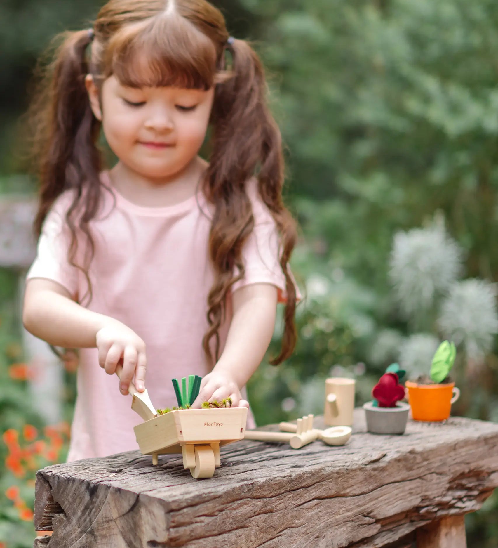 Child playing with a PlanToys garden wheelbarrow set on a wooden bench. 