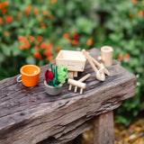 PlanToys wooden wheelbarrow next to other garden tools and loose veg pieces on a bench in the garden