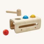 The PlanToys wooden Hammer Ball play set has a rounded base to allow for movement when the balls are being hammered through the holes. There are two wooden horizontal sticks in the underside of the hammer bench to allow the balls to run out and be collected. The balls are red, blue and yellow and there is a wooden hammer/mallet above the hammer board.