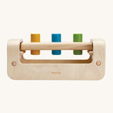 A view from the side of the PlanToys Pounding Bench, showing the rounded base and the 3 pegs half way through the holes. The pegs are yellow, blue and green, and the mage is on a cream background
