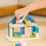 Back of PlanToys wooden blue house set showing child's hand picking up a mother wooden figure