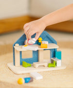 Back of PlanToys wooden blue house set showing child's hand picking up a mother wooden figure