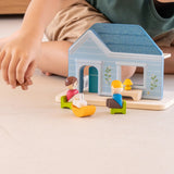 PlanToys wooden blue house set standing on a concrete surface with a child in the background
