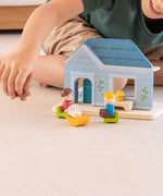 PlanToys wooden blue house set standing on a concrete surface with a child in the background