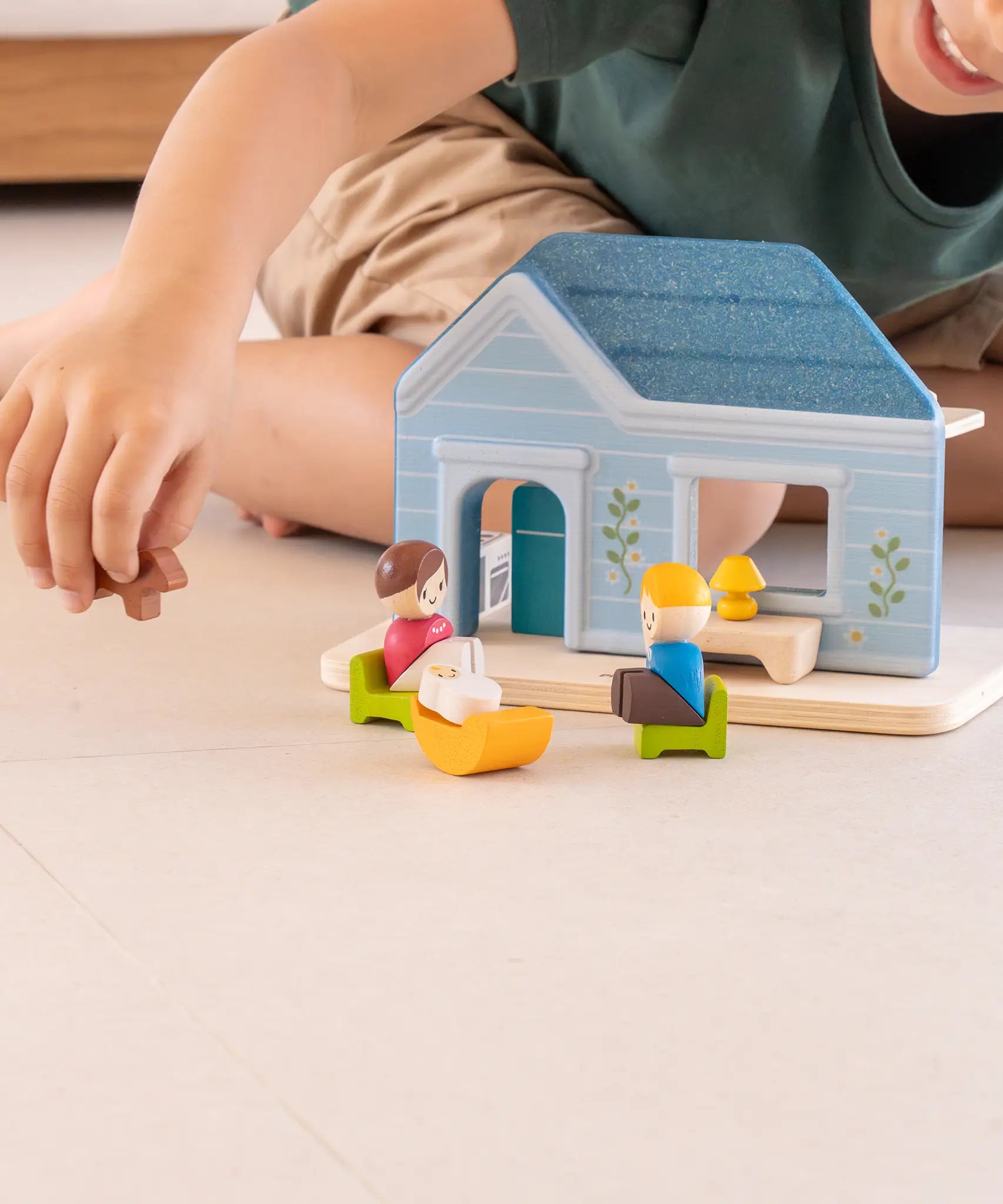 PlanToys wooden blue house set standing on a concrete surface with a child in the background